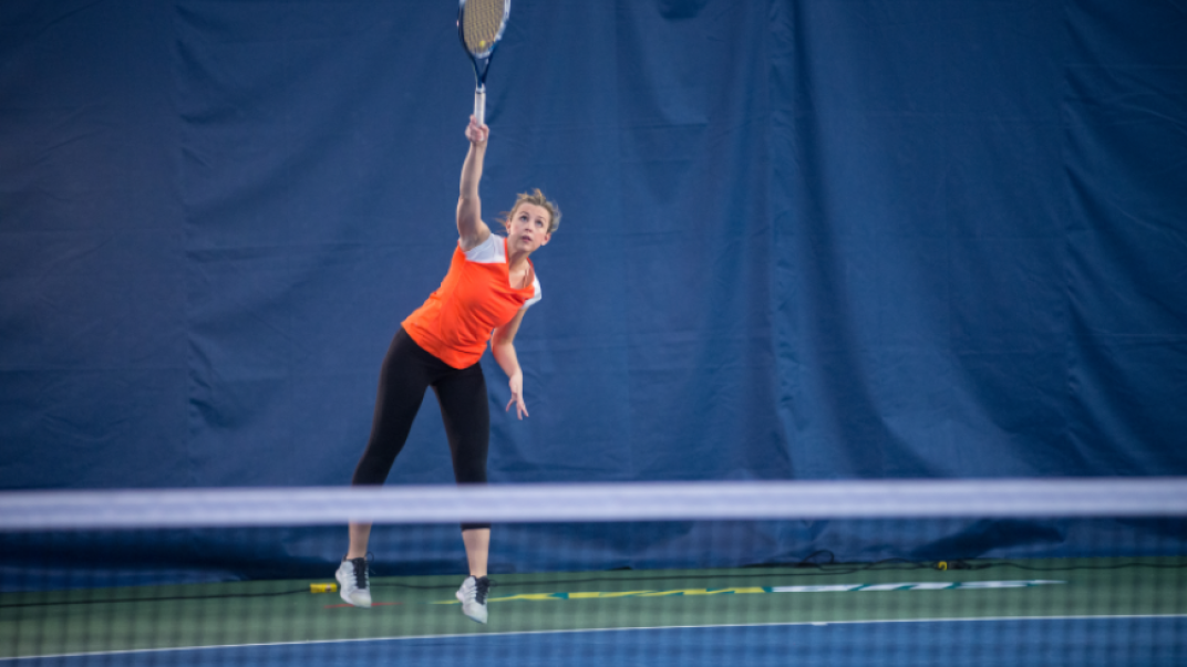 Woman in orange shirt playing tennis at a tennis court.