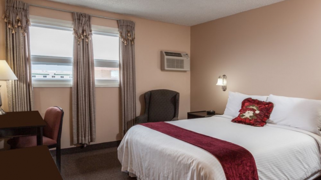 hotel room with a queen bed, white bedding and red throw pillow