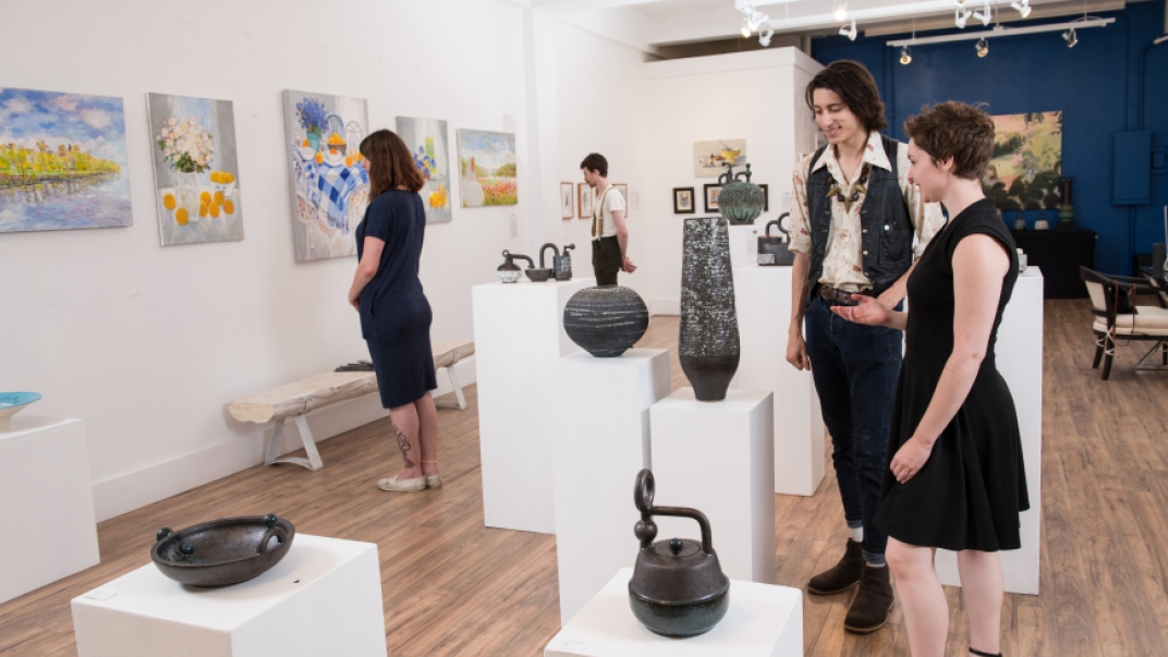 four people in a gallery viewing colourful paintings and black pottery