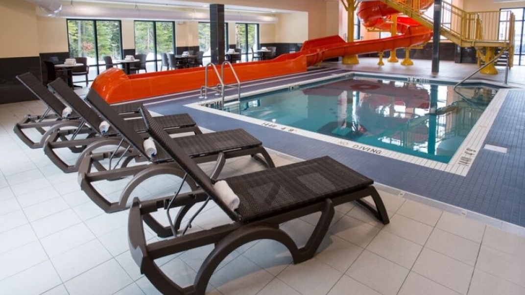 Image of an indoor pool with a red waterslide and lounge chairs on the pool deck