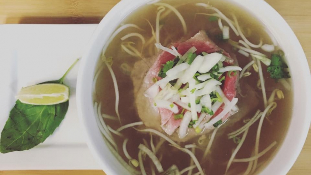 White bowl of noodle and meat in broth on a table