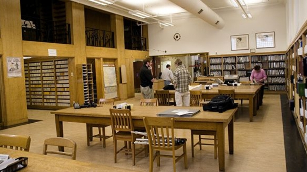 Archival library interior. There are some desks and chairs as well as bookcases filled with archival documents.