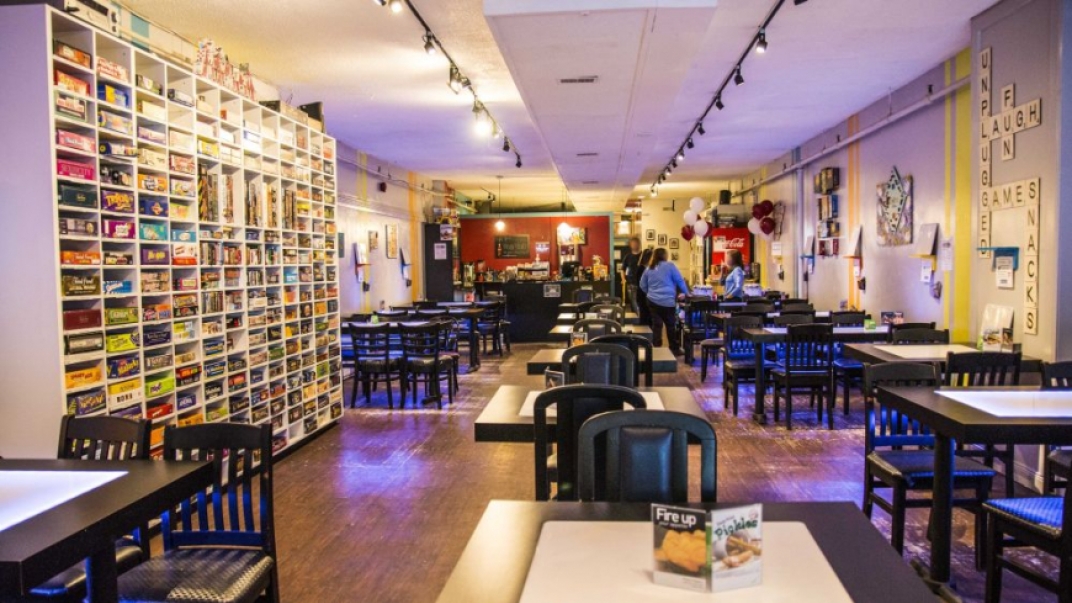 Interior of board game cafe. There a chairs and tables throughout the room and shelving with board games in it