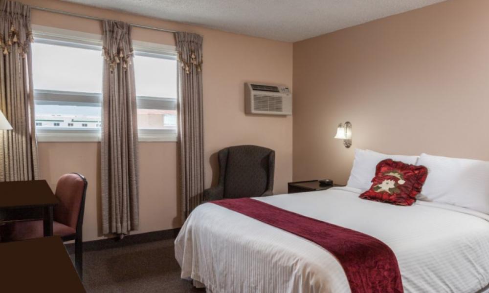 hotel room with a queen bed, white bedding and red throw pillow