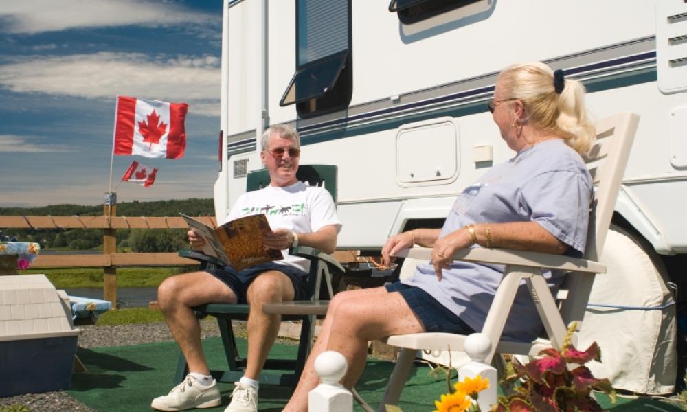 Smiling elderly couple sits on lawn chairs in front of an RV. 