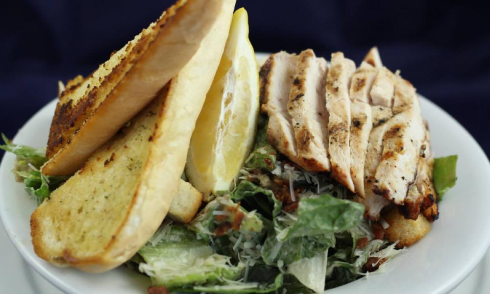 plate of chicken caesar salade and garlic bread